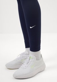 Hvide Nike sneakers med en struktureret overflade, parret med navy leggings med en subtil hvid Nike swoosh-logo. Elastiske ankler.