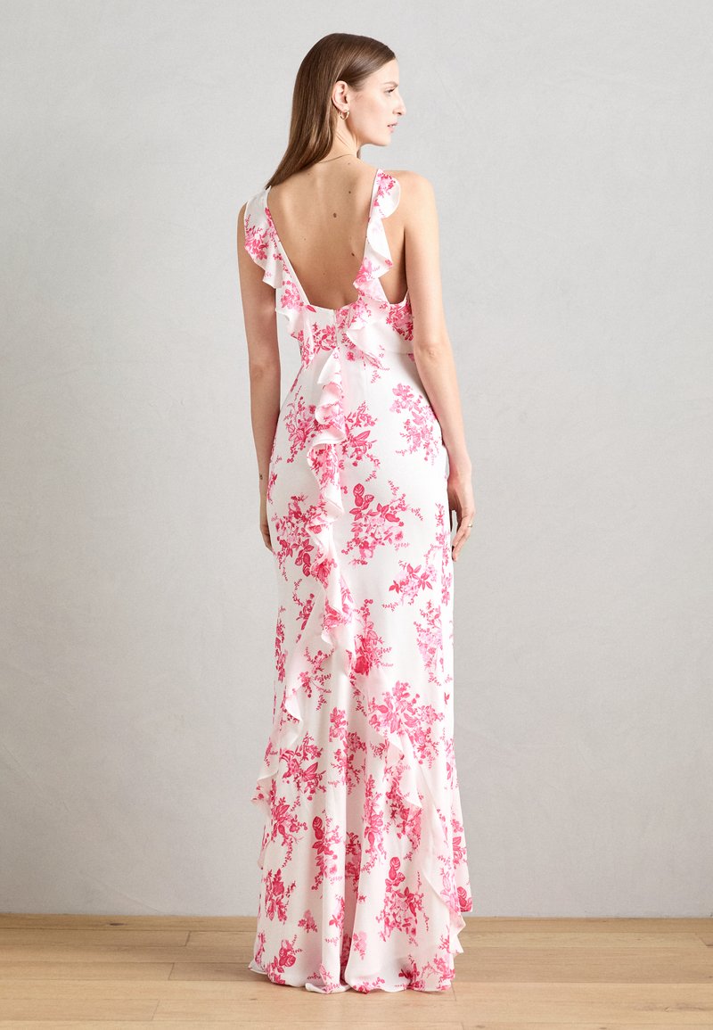 Robe florale blanche avec des motifs roses, dotée de bretelles froncées et d'un dos élastiqué, taille cintrée et un design fluide jusqu'au sol.