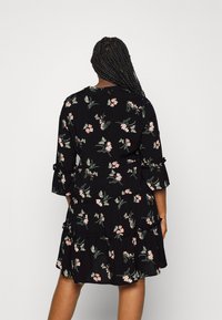 Black dress with floral and butterfly patterns, featuring three-quarter sleeves, ruffled hem, and a relaxed fit. Made of lightweight fabric.