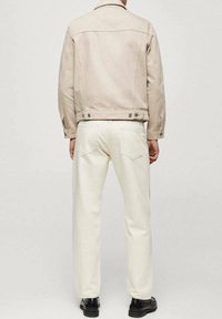 Chaqueta de mezclilla beige con un cuello estructurado y detalles de botones, combinada con jeans de pierna recta color blanco sucio y zapatos negros.