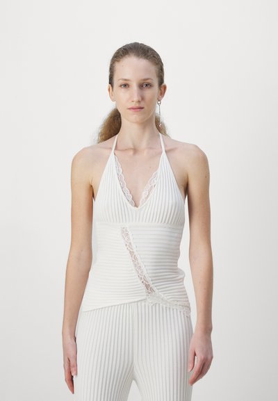 Débardeur blanc à côtes avec un col halter. Présente une bordure en dentelle le long de l'encolure et un accent en dentelle angulaire à la taille.
