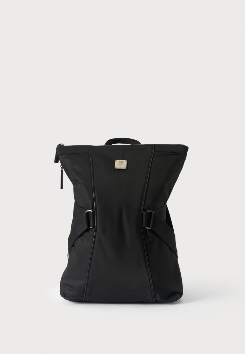 Sac à dos noir avec fermeture éclair sur le dessus, poignée de transport, sangles latérales réglables et une petite plaque métallique carrée avec logo au centre devant.
