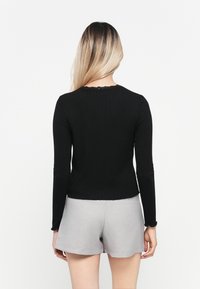 Svart langermet topp med ribbet tekstur og blondekant ved halsen, sammen med grå shorts som er synlige nederst.