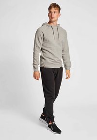 Grå hættetrøje med snor, tekstureret stof, kombineret med sorte joggingbukser. Outfit'et fuldendes med sorte sportssko med røde detaljer.