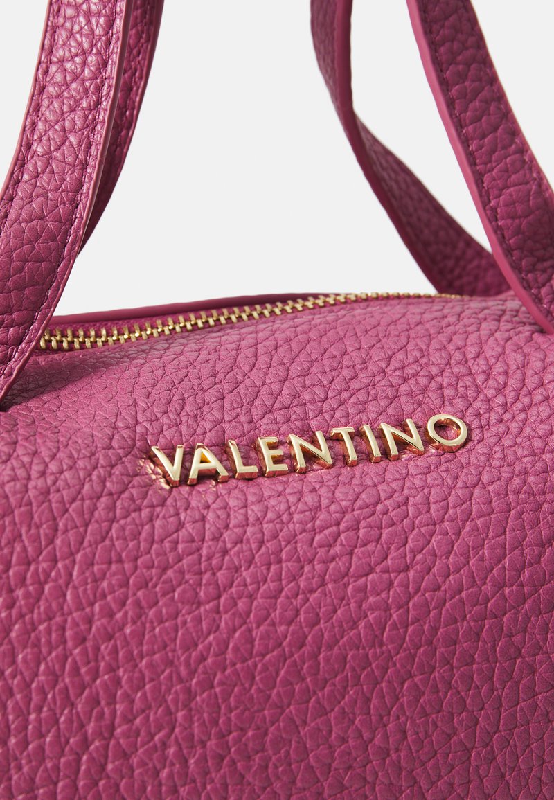 Rosa Lederhandtasche mit strukturiertem Oberflächen, goldenem Reißverschluss und Logo-Akzent. Verfügt über zwei Griffe und ein kompaktes Design.
