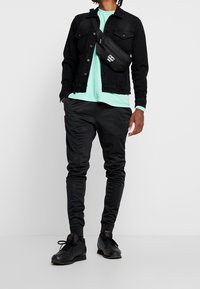 Musta farkkutakki, vaaleanvihreä t-paita, mustat treenihousut ja mustat tennarit, joissa on punaisia yksityiskohtia. Pieni musta olkalaukku, joka on yllään ristikkäin.