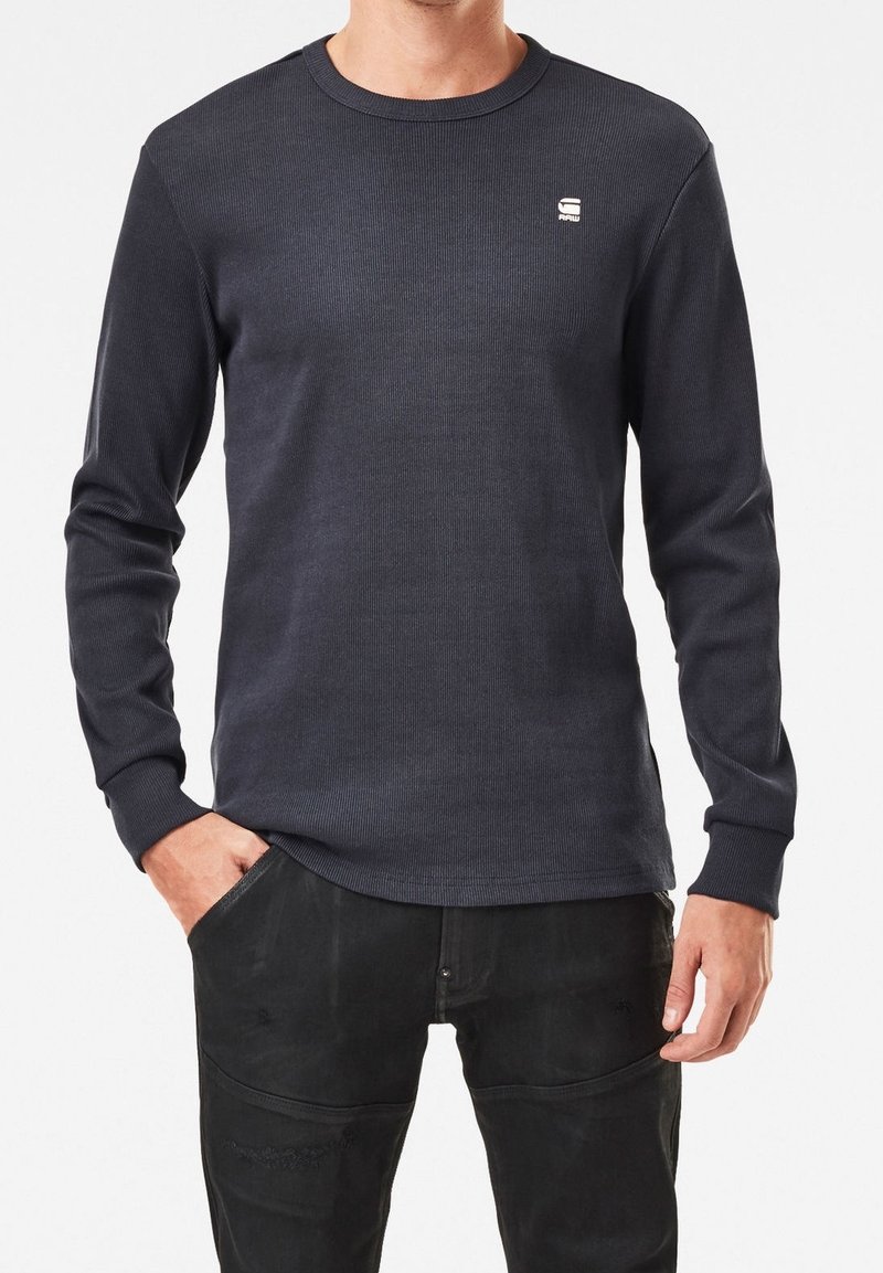 Mörk marinblå långärmad ribbad crewneck sweatshirt med en liten logga på bröstet, med åtsittande mudd och en avslappnad passform.