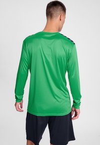 Groene lange mouwen sportshirt met een gladde textuur en ronde hals, met zwarte accentstrepen op de schouders. Draag het met zwarte shorts.