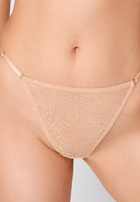 Beżowe stringi wykonane z miękkiego, teksturowanego materiału, z cienkimi paskami i trójkątnym kształtem, oferującym minimalne pokrycie.