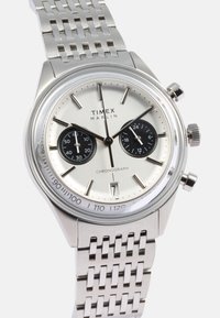 Silver stainless steel watch with a chronograph feature, black sub-dials, polished bezel, and a woven metallic bracelet.