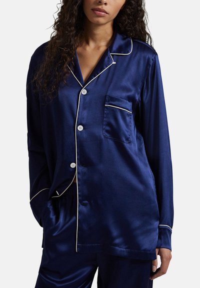 Marineblauw satijnen pyjamaset met een overhemd met knopen, witte biezen en een borstzak. Heeft lange mouwen en een ontspannen pasvorm.