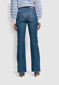 Blaue Schlagjeans aus Denim, mit hoher Taille, fünf Taschen und sichtbaren Nähten, kombiniert mit einem gestreiften Pullover.