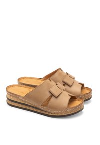 Beżowe skórzane klapki z dwoma ozdobnymi kokardami, odkrytą toe i perforowanymi detalami. Półśrodkowa podeszwa w stylu korka z brązową gumową podeszwą.