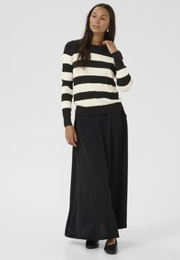 Pull rayé noir et crème en mélange de laine, avec des manches longues et un col rond, associé à une jupe maxi noire et des chaussures plates.
