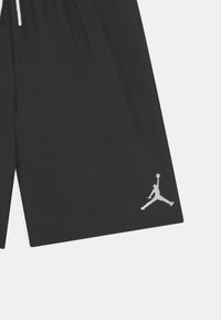 Pantalones cortos deportivos negros con una cinturilla elástica, que presentan un logo blanco de Jumpman en el lado izquierdo y una textura de tela suave.