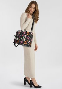 Borsa tote intrecciata nera con motivi floreali colorati. Presenta una maniglia superiore e una tracolla regolabile. Texture liscia con accenti a contrasto.