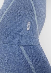 Niebieskie legginsy sportowe wykonane z teksturowanej tkaniny z kontrastującymi jasnoniebieskimi szwami. Posiadają małą metkę z logo wszytą w materiał.