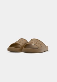 Sandales en caoutchouc marron avec un bout ouvert, présentant une semelle texturée et un logo en relief sur la sangle supérieure.