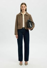 Chaqueta corta de ante marrón con gran cuello, camisa crema, jeans azul oscuro y bolso negro con detalle de cinta. Tacones beiges de punta.