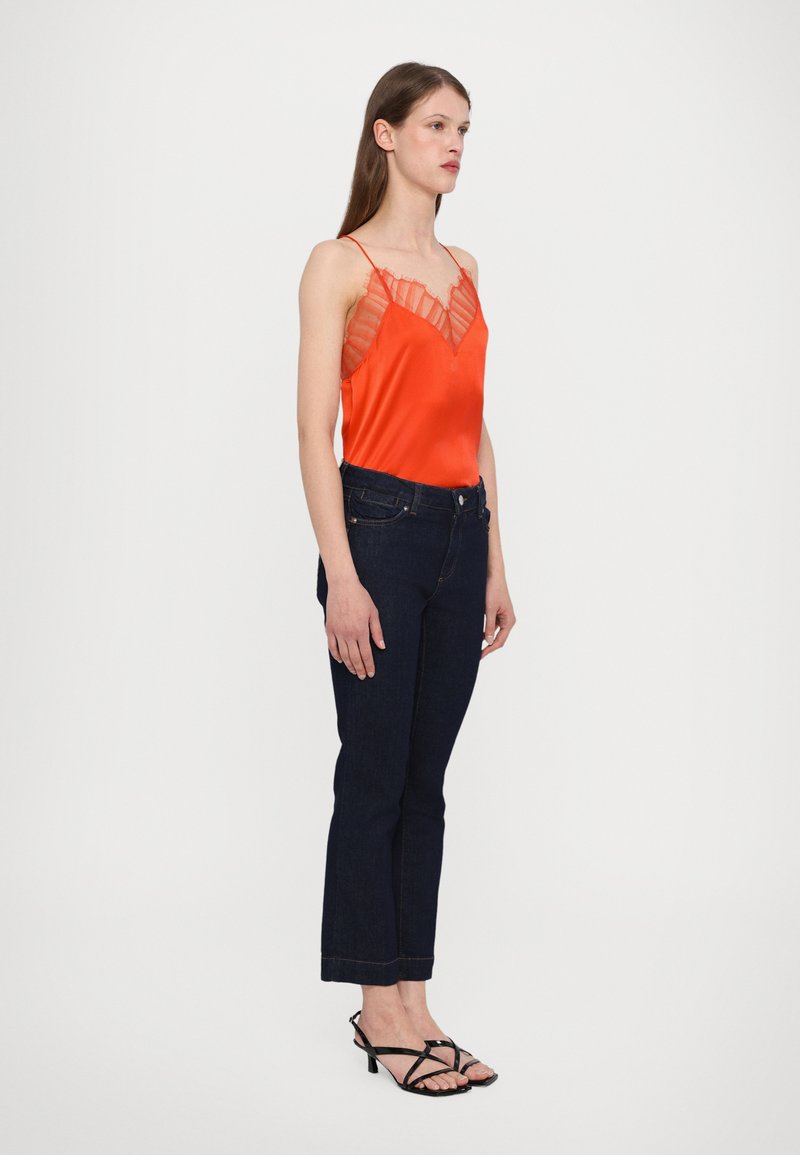 Red satin camisole with lace trim, paired with dark blue jeans. Model wears black strappy heels. Straight-cut jeans with cuffed hems.