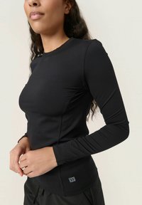 Top fitted a maniche lunghe nera realizzato in materiale elastico, con cuciture piatte e un piccolo logo vicino all'orlo. Texture liscia.
