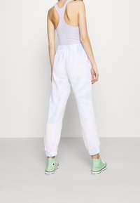 Joggers de tie-dye en tonos pastel con cintura elástica y tobillos ajustados, combinados con una camiseta sin mangas de color púrpura claro y zapatillas altas verdes.