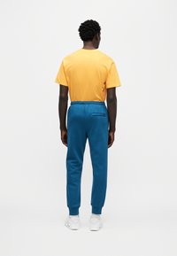 Πορτοκαλί βαμβακερό t-shirt συνδυασμένο με μπλε φόρμα με ελαστική μέση και πίσω τσέπη. Το σύνολο ολοκληρώνουν λευκά αθλητικά παπούτσια.