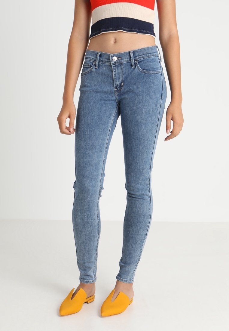 Femme portant un jean skinny bleu clair, un top court rouge, blanc et bleu marine, et des chaussures slip-on jaune vif à bouts pointus.