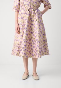 Gonna midi floreale realizzata in tessuto leggero, con una base rosa e fiori viola e verdi, vita cinchata e forma a A.