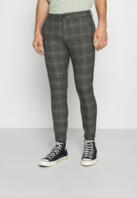 Grå rutig byxor med smal passform och mjuk textur, med knappstängning och sidofickor, kombinerat med svarta högstövlar.