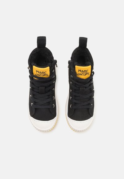 Sneaker alte nere con logo giallo e nero, puntale in gomma bianca, lacci neri e tomaia in tessuto testurizzato. Presenta un occhiello sul tallone.