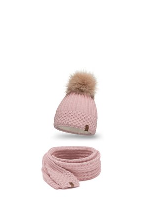 Un bonnet en tricot rose avec un pompon en fourrure et une écharpe assortie. Les deux présentent un motif texturé et une petite étiquette marron sur le bonnet.