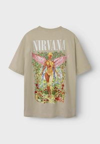 Camiseta beige con un vibrante estampado gráfico en la parte posterior que representa una figura con alas, rodeada de flores, relojes y vegetación.