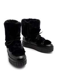 Botas forradas de piel negra con puntera de cuero negro brillante y suela de plataforma gruesa. Cuentan con cordones y una cremallera para el cierre.