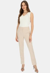 Beżowe dopasowane spodnie z subtelnymi pionowymi paskami, w połączeniu z białą bezrękawną bluzką z dekoltem w serek i gładką teksturą.
