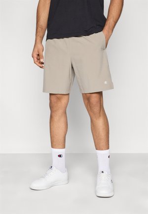 Pantalones cortos deportivos beige con cintura elástica, con el logotipo de Champion en la pierna izquierda. Combinados con zapatillas blancas y calcetines.