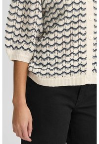 Krämfärgad cardigan med marinblå vågmönster, lös passform, knäppning med knappar och ribbad nederkant. Tillverkad av lätt stickad tyg.