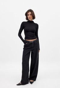 Crn dolg rokav turtleneck top, v kombinaciji z ohlapnimi črnimi kavbojkami z razpršeno pikasto vzorčno in pasom s srebrno zaponko.