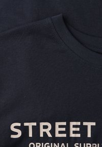 Granatowy bawełniany T-shirt z okrągłym dekoltem i dużym kremowym napisem "STREET ORIGINAL SUPPLY" na przodzie.