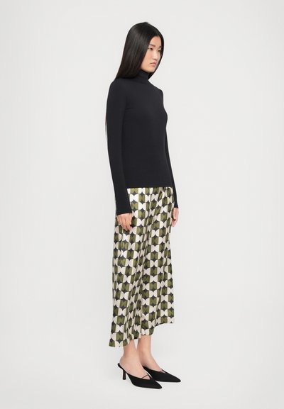 Zwarte coltrui met lange mouwen, gecombineerd met een groene gebloemde rok met geometrische ontwerpen. Zwarte puntige hakken maken de look compleet.