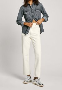 Denimskjorta med knappar och två bröstfickor, vita hög midja vida byxor och sneakers i silverfärg med mönstrade detaljer.