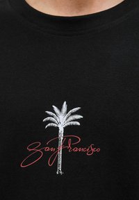 Juodas marškinėliai su baltu palmės grafiką ir raudonu šriftu "San Franciskas" apačioje. Lygus audinys, apvalus iškirpimas.