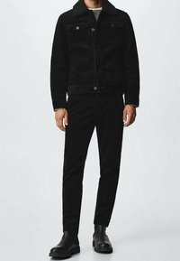 Sort fløjlsjakke og bukser set, med en tekstureret overflade. Sættet er suppleret af sorte ankelstøvler, hvilket skaber et monokromatisk look.