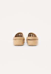 Tan rubber clogs with ventilation holes, back strap, and textured soles. Simple design with a rounded shape, suitable for casual wear.