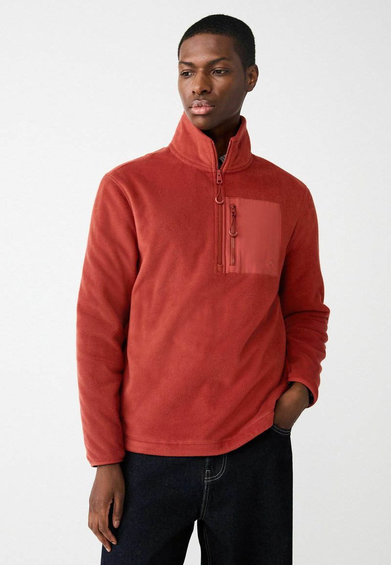 Roter Fleece-Pullover mit hohem Kragen, Halb-Reißverschluss auf der Vorderseite und einer Brusttasche in passender Farbe. Weiche Textur, lässige Passform.