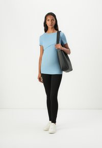 Lys blå ribbet graviditetstopp med korte ermer, buet sømdetalj, kombinert med svarte leggings og en svart tote bag. Hvite joggesko.