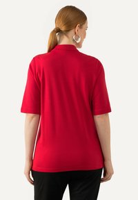Polo de manga corta rojo en suave material de algodón, que presenta un cuello clásico y un corte recto con un diseño liso en la parte trasera.