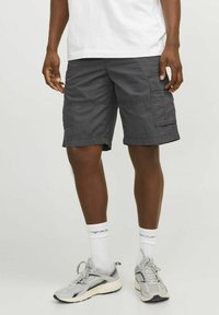 Shorts cargo gris avec poches latérales, fabriqués en tissu léger. Associés à des baskets grises et des chaussettes blanches arrivant à la cheville. Design simple et pratique.