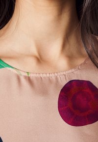 Hedvábná látková blůza s kulatým výstřihem, růžovým základem, zelenými a tmavě modrými akcenty a velkými kruhovými vzory v červené a vínové barvě.