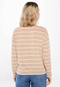 Beige tröja med vita horisontella ränder, med en avslappnad passform och långa ärmar. Mjuk textur och rund halsringning, matchad med blå jeans.